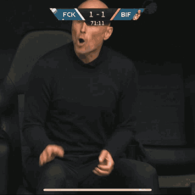 a man sitting in a chair with his fist in the air watching a soccer game between fck and bif