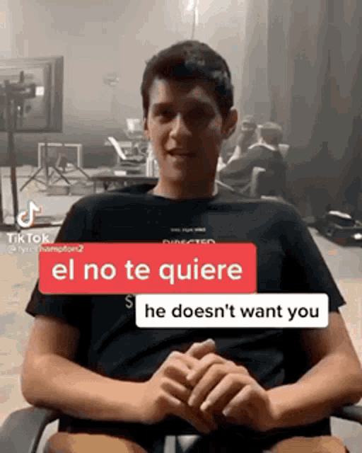 a young man in a black shirt is sitting in a chair with a red sticker that says " el no te quiere "