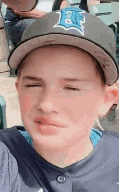 a young boy wearing a hat and a blue shirt is making a funny face .