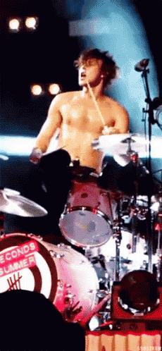 a shirtless man is playing drums in front of a drum set that says seconds summer on it