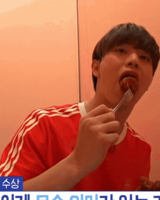 a man wearing a red adidas shirt is eating a piece of meat with a fork