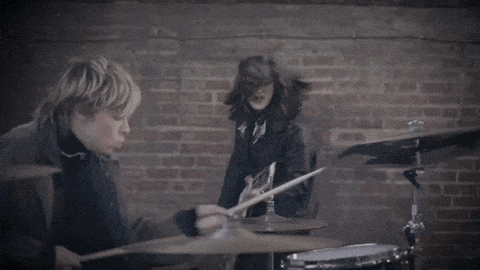 a man is playing drums while a woman plays guitar in front of a brick wall