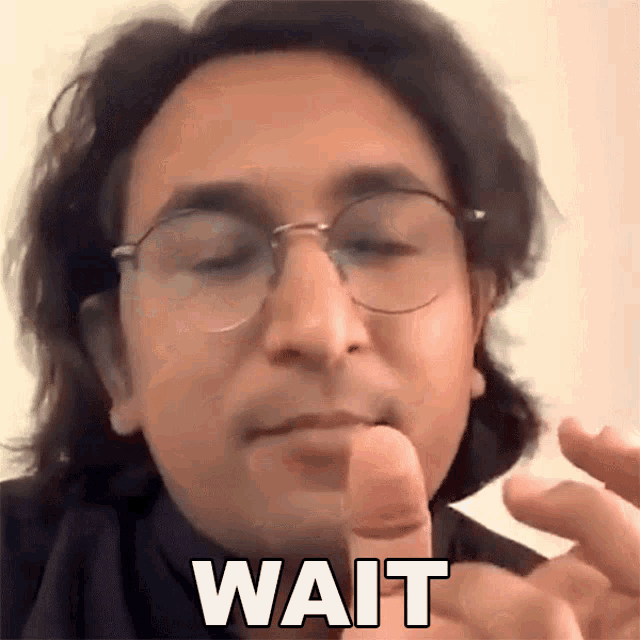 a man wearing glasses is making a funny face and the word wait is on his face