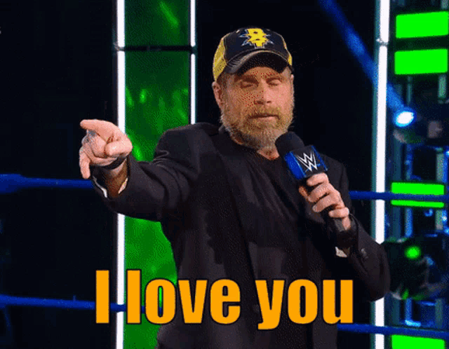 a man holding a microphone and pointing with the words i love you behind him