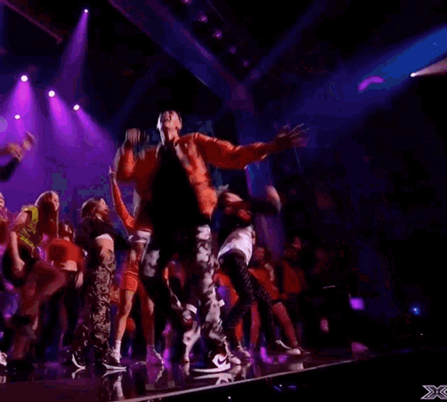 a group of people are dancing on a stage with purple lights behind them .