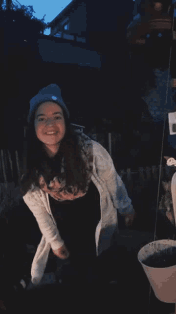 a woman wearing a green beanie and a white cardigan smiles for the camera
