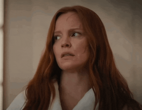 a woman with red hair is wearing a white shirt and making a surprised face