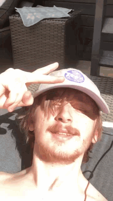 a man with a beard wearing a white hat with a blue logo on it giving a peace sign