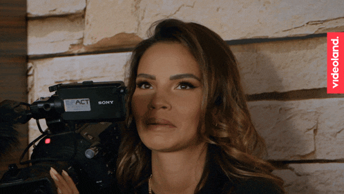 a woman is holding a sony camera in front of a stone wall