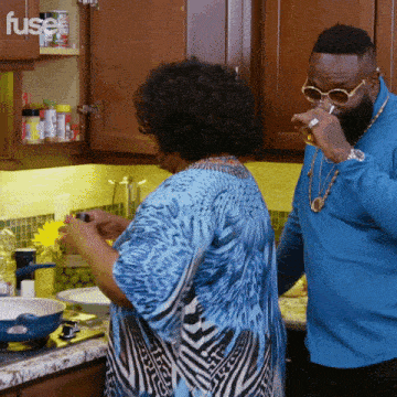 a man in a blue shirt is drinking from a glass while standing next to a woman in a blue top