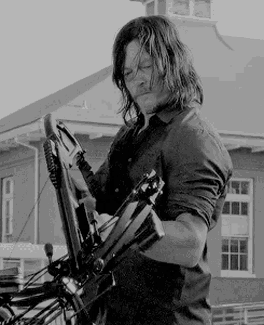 a man with long hair is holding a bow and arrow in front of a building .