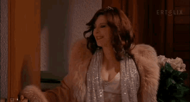 a woman in a fur coat is standing in front of a door and smiling .