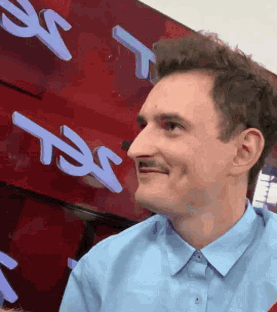 a man in a blue shirt is smiling in front of a red sign that says tsx