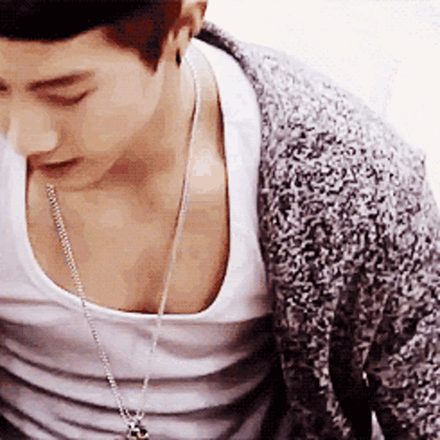 a young man wearing a white tank top and a necklace
