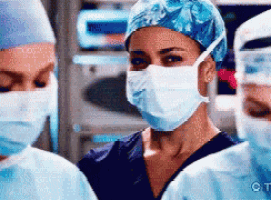 a woman wearing a surgical mask and a blue hat is standing next to two other surgeons