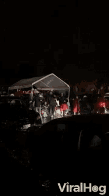 a group of people are standing under a tent in a parking lot .