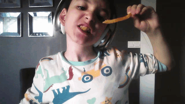a young boy wearing headphones is eating a french fry
