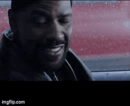 a man is smiling in a car with a red car in the background