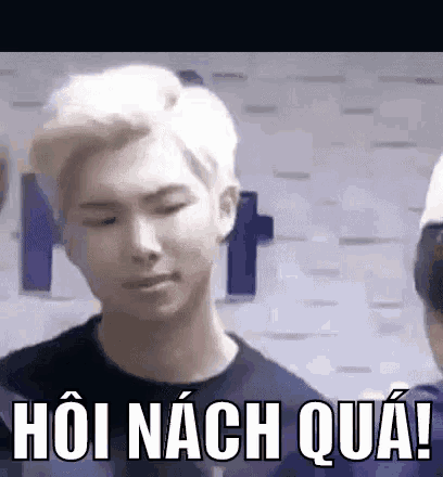 a man with blonde hair is standing in front of a wall with a foreign language written on it .