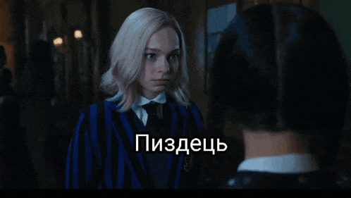 a woman in a blue and black striped jacket is talking to another woman in a dark room in a foreign language