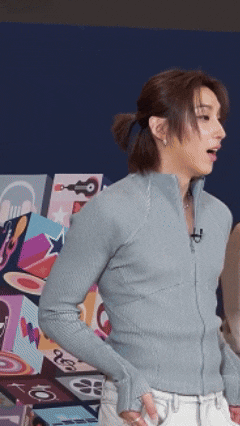 a man with a ponytail is wearing a light blue sweater and white jeans