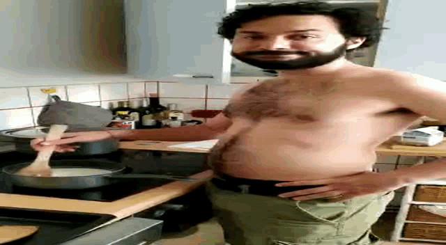 a shirtless man with a beard is cooking in a kitchen with a wooden spoon .