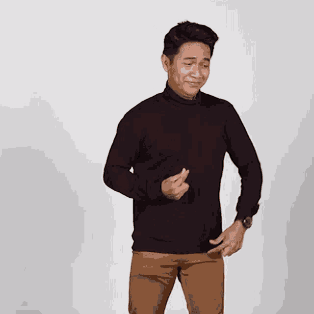 a man wearing a black sweater and brown pants smiles