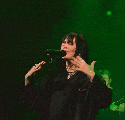 a woman singing into a microphone in a dark room with a green light behind her