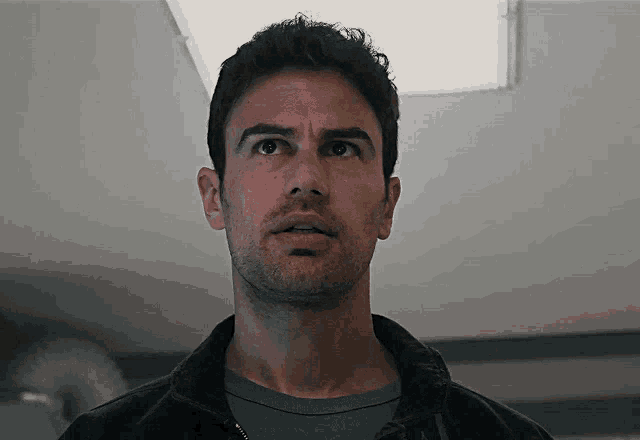 a man with a beard and a black jacket looks up at something