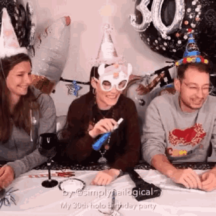 a group of people are sitting at a table wearing party hats and glasses .