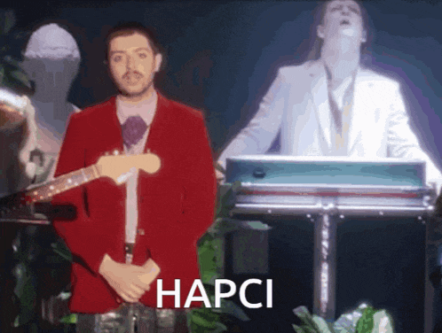 a man in a red jacket is playing a guitar and the word hapci is on the bottom right