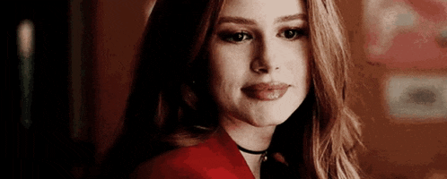 a close up of a woman wearing a red jacket and a choker looking at the camera .