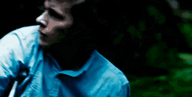 a man in a blue shirt is standing in the dark .