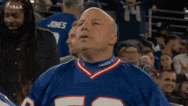 a man wearing a giants jersey is sitting in the stands watching a game .