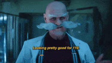 a bald man with a mustache and a white coat says looking pretty good for 110