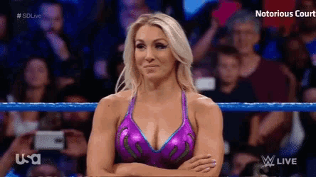 a woman in a purple top is standing in a wrestling ring with her arms crossed