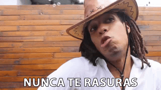 a man with dreadlocks wearing a cowboy hat and a white shirt says nunca te rasuras