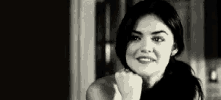 a woman is smiling in a black and white photo with her hand on her chin .