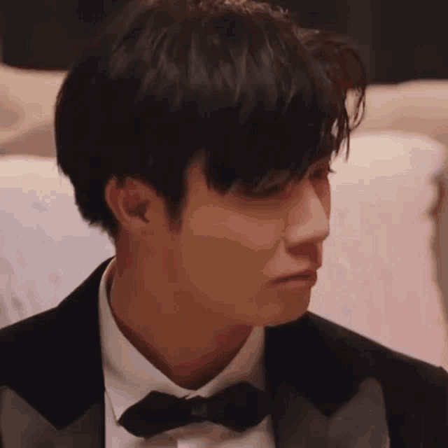 a man in a tuxedo and bow tie is crying while sitting on a couch .