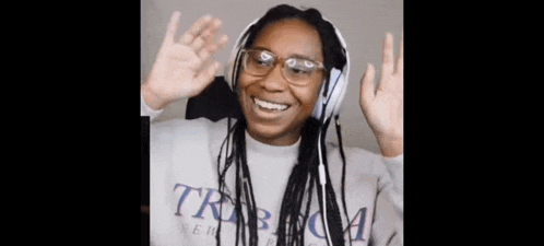 a woman wearing headphones and glasses is smiling and waving her hands in the air .