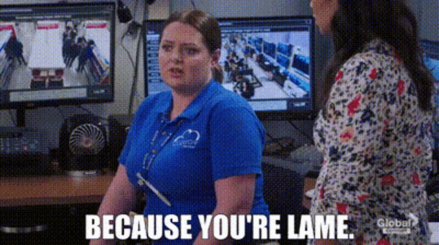a woman in a blue shirt is sitting at a desk in front of a computer and a monitor .