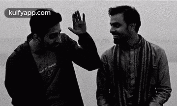 two men are standing next to each other and waving at each other .