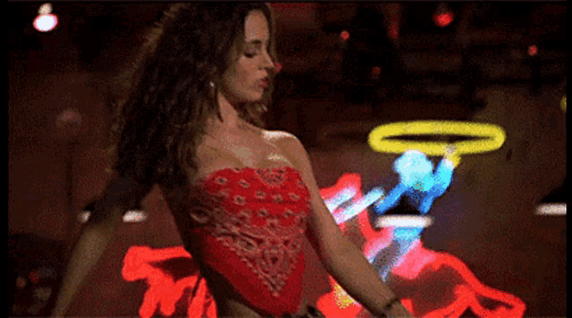 a woman in a red strapless top is dancing in front of a neon sign