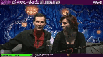 a man and a woman are standing in front of a screen that says " happy halloween "