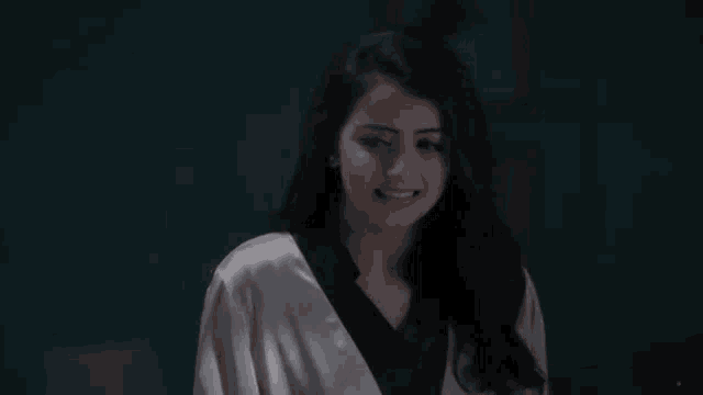 a woman in a white robe and black top is smiling in a dark room .