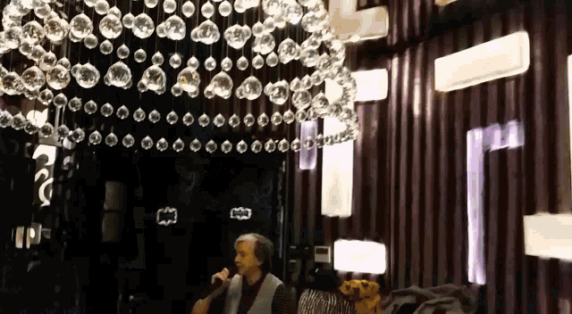 a man is sitting in front of a chandelier with a fox logo on his shirt