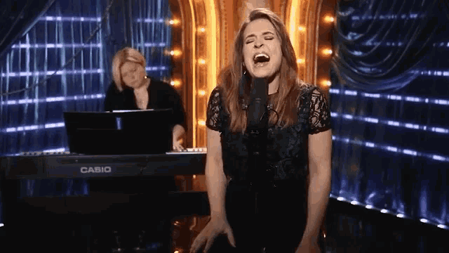 a woman singing in front of a casio piano
