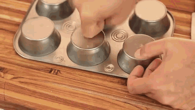 a person is making cupcakes in a muffin pan on a wooden counter .