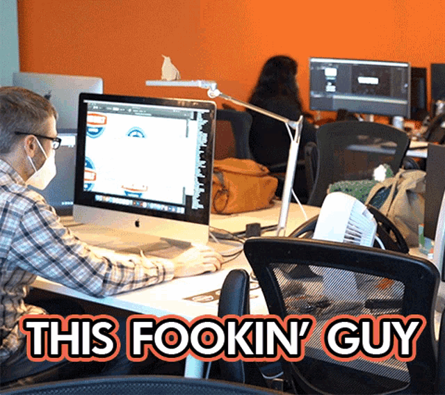 a man wearing a mask sits at a desk in front of a computer with the words this fookin ' guy below him