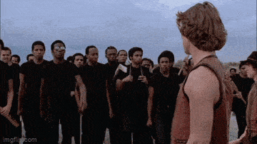 a man in a red tank top is standing in front of a group of men in black shirts .